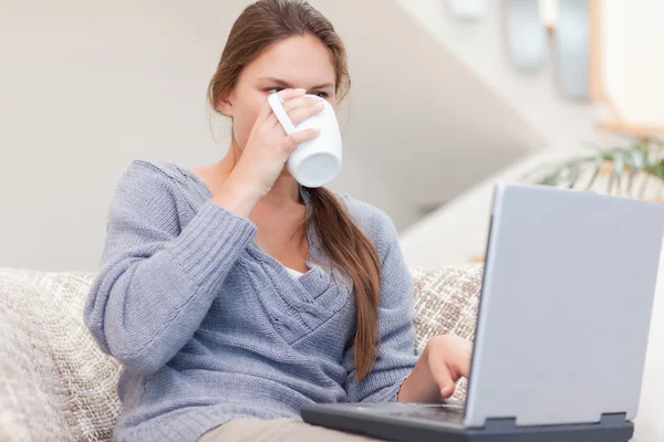 Γυναίκα χρησιμοποιώντας ένα φορητό υπολογιστή, πίνοντας ένα φλιτζάνι τσαγιού — Φωτογραφία Αρχείου