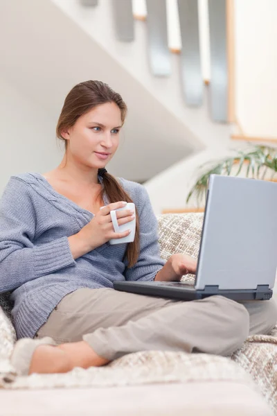 Retrato de uma mulher usando um laptop enquanto toma um chá — Fotografia de Stock