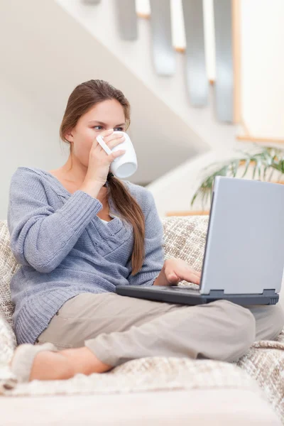 Retrato de uma mulher usando um laptop enquanto bebe uma xícara de chá — Fotografia de Stock