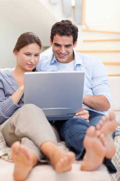 Retrato de um casal usando um laptop enquanto estava deitado em um sofá — Fotografia de Stock