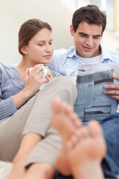 Couple reading a newspaper while lying on a sofa — Stock Photo, Image