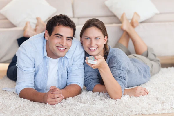 Linda pareja viendo la televisión mientras está acostada en una alfombra — Foto de Stock