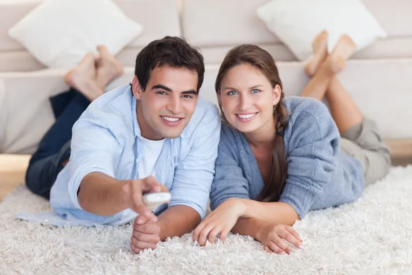 Couple souriant regardant la télévision tout en étant allongé sur un tapis — Photo