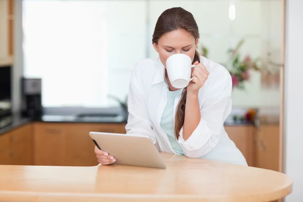Woman using a tablet computer while drinking coffee — Stock Photo, Image
