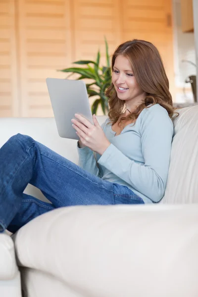 微笑着与她平板电脑在沙发上的女人 — 图库照片