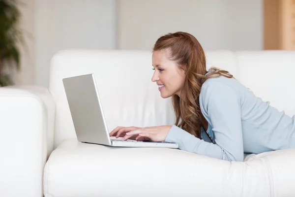 Mujer joven en el sofá escribiendo en su computadora portátil — Foto de Stock