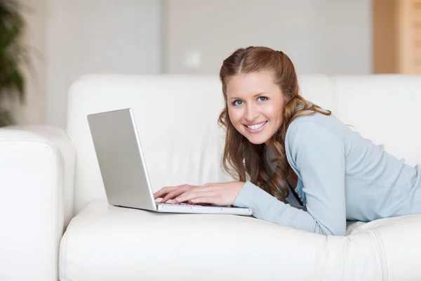 Mulher sorridente alegre no sofá digitando em seu laptop — Fotografia de Stock
