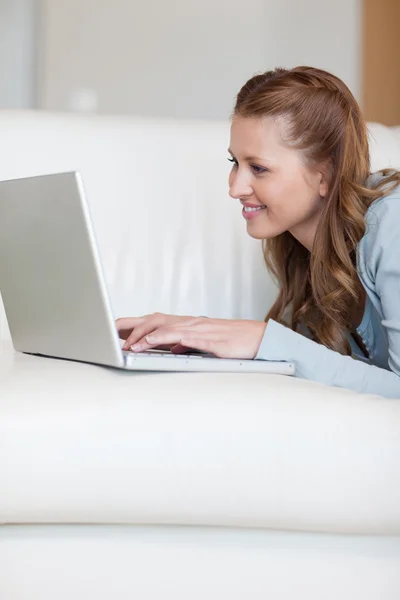 Sorrindo jovem fêmea com laptop no sofá — Fotografia de Stock