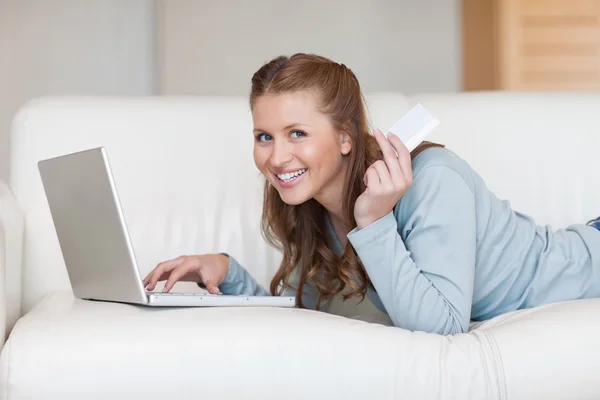Donna sorridente sul divano con la sua carta di credito online — Foto Stock