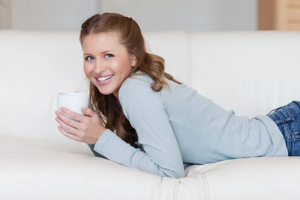 Ung kvinna njuter av en kaffe paus på hennes soffa — Stockfoto