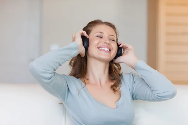 Χαμογελώντας γυναίκα απολαμβάνετε τη μουσική στον καναπέ — Φωτογραφία Αρχείου