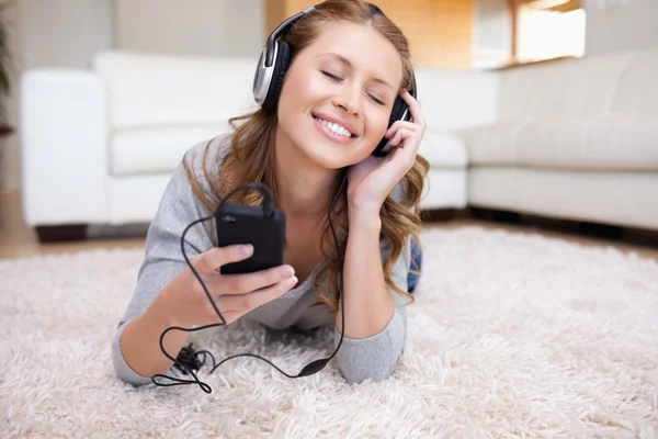 音楽を聴くのカーペットに横たわって若い女性 — ストック写真