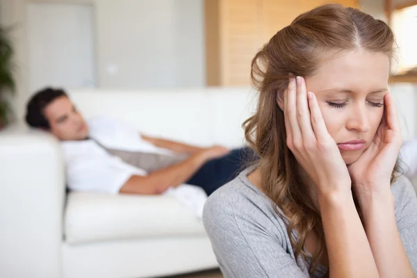 Женщина испытывает головную боль с мужчиной на диване позади нее — стоковое фото