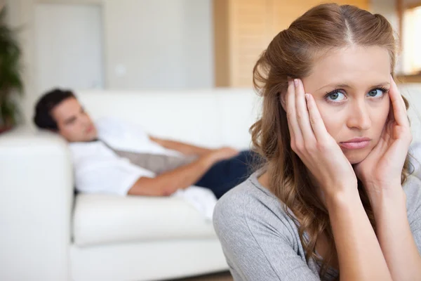 Женщина страдает от головной боли с мужчиной на диване позади нее — стоковое фото