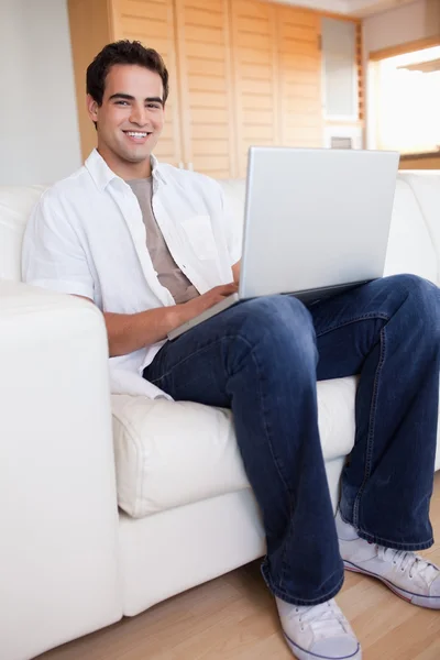 笔记本电脑在沙发上微笑着男性 — 图库照片