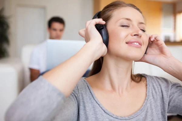 Woman listening to music with man sitting behind her on the sofa — Stock Photo, Image