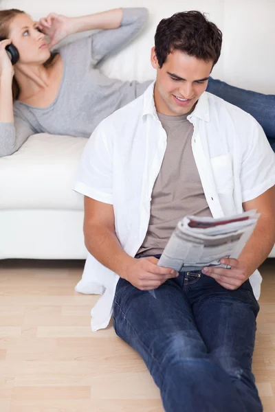 Мужчина читает новости, пока его девушка слушает музыку — стоковое фото