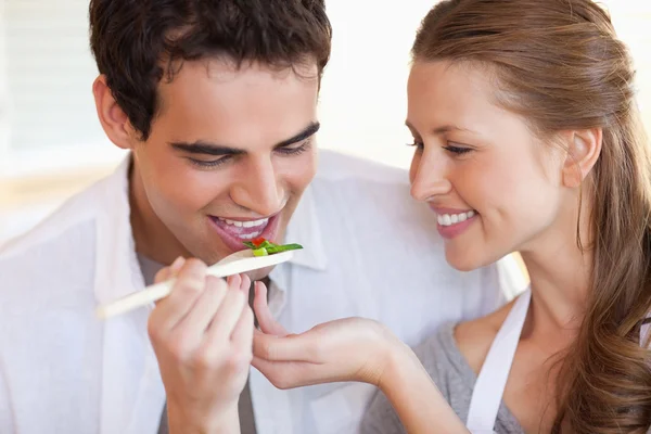 Homem está provando a refeição que sua namorada está cozinhando — Fotografia de Stock