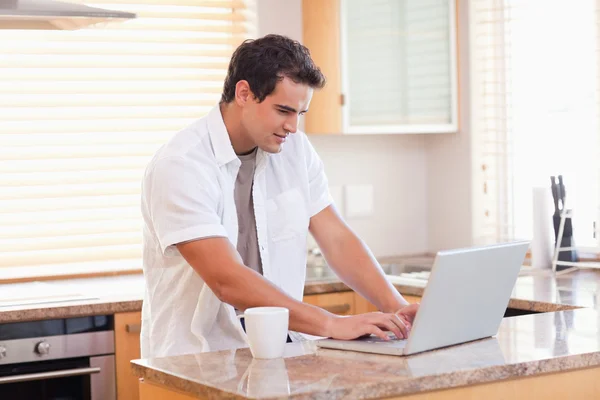 Mann arbeitet in der Küche an seinem Laptop — Stockfoto
