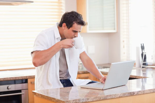 Человек с кофе и ноутбуком на кухне — стоковое фото