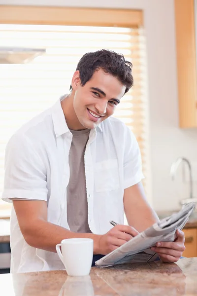 Sorrindo homem fazendo palavras cruzadas na cozinha — Fotografia de Stock