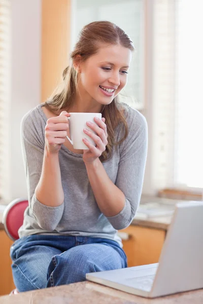Женщина пьет кофе, глядя на свой ноутбук — стоковое фото