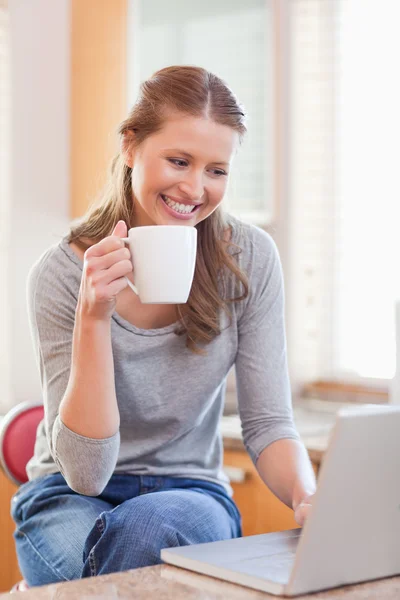 Χαμογελώντας γυναίκα απολαμβάνοντας καφέ δακτυλογραφώντας για το laptop — Φωτογραφία Αρχείου