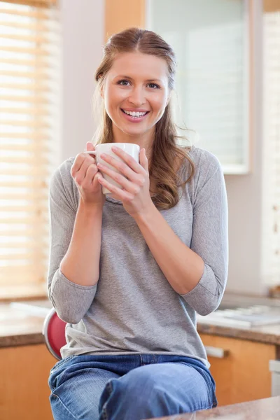 Mujer sonriente tomando una taza de café en la cocina — Foto de Stock