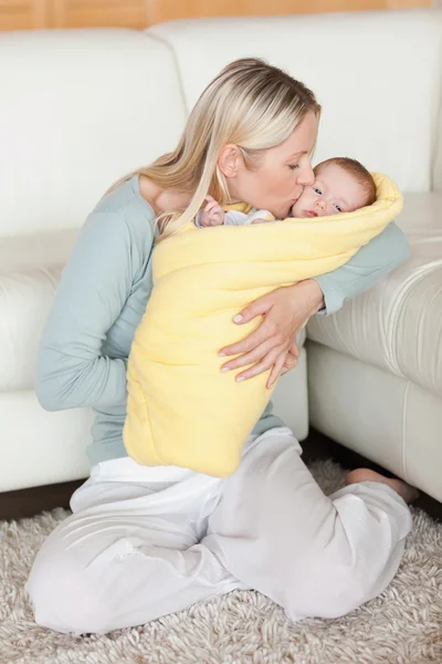 Mãe beijando seu bebê que está embrulhado em uma capa — Fotografia de Stock