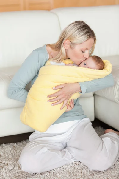 Любящая мама целует своего ребенка, который завернут в обложку — стоковое фото