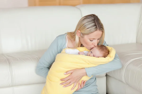 Krásná matka líbat její dítě, který je zabalen do cover — Stock fotografie