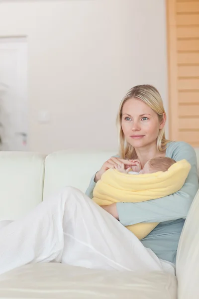 Mother sitting on the couch while holding her baby — Stock Photo, Image