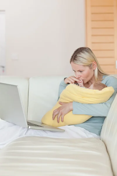 Mother looking at her laptop while holding her baby — Stock Photo, Image