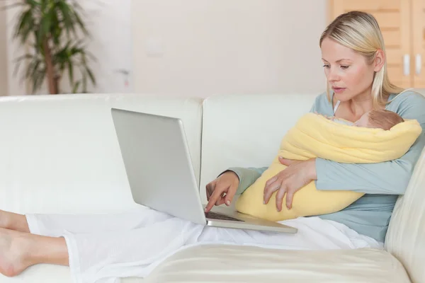 Mother surfing the internet while holding her baby — Stock Photo, Image