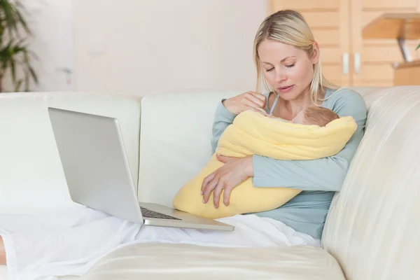 Madre con cuaderno en el sofá sosteniendo a su bebé — Foto de Stock