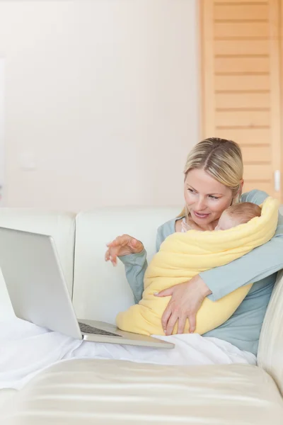 Mãe no sofá mostrando ao bebê algo no laptop — Fotografia de Stock