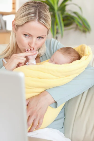 Mother kissing her baby's hand while looking at the laptop — Stock Photo, Image