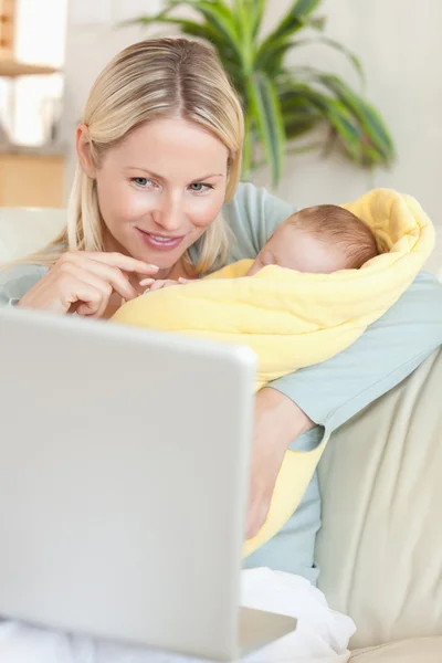 Moeder in de woonkamer met haar baby kijken naar haar laptop — Stockfoto