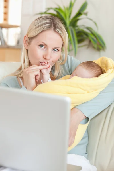 Mother kissing her baby's hand while sitting on the sofa — Stock Photo, Image