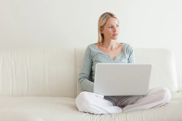 Жінка сидить хрест ногами на дивані з ноутбуком — стокове фото