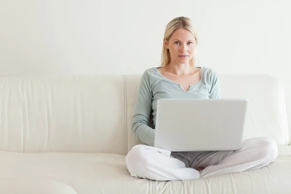Kvinna sitter cross ben i soffan med sin bärbara dator — Stockfoto
