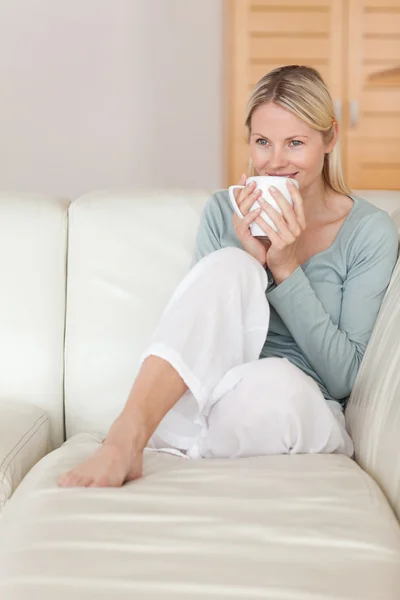 Frau nimmt einen Schluck Kaffee auf dem Sofa — Stockfoto