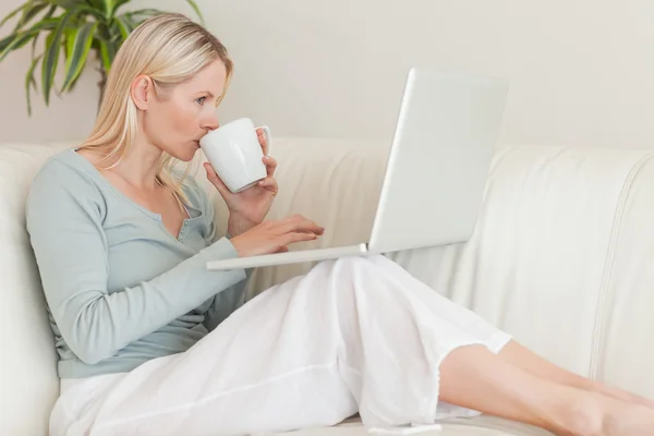 Mujer disfrutando de un sorbo de café mientras trabaja en su computadora portátil — Foto de Stock