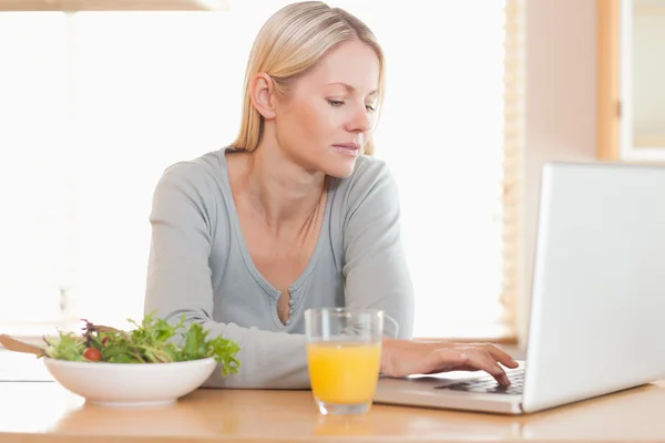 Frau isst gesundes Mittagessen, während sie am Laptop arbeitet — Stockfoto