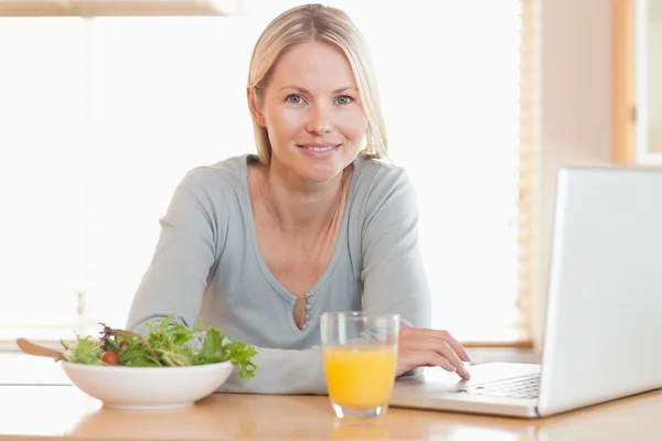 Frau isst gesundes Mittagessen, während sie an ihrem Notizbuch arbeitet — Stockfoto