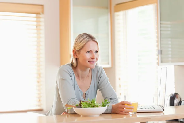 Mujer con ensalada y portátil en la cocina con un vaso de o — Foto de Stock
