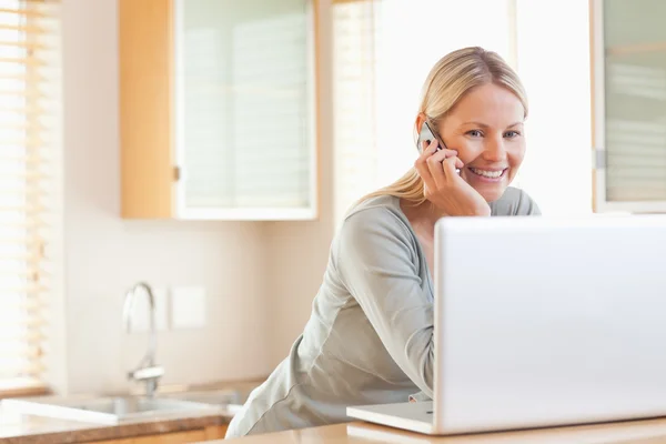 Mujer sonriente en el teléfono mirando su computadora portátil — Foto de Stock