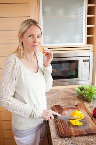 Side view of woman trying some bell pepper while cutting it — Stock Photo, Image