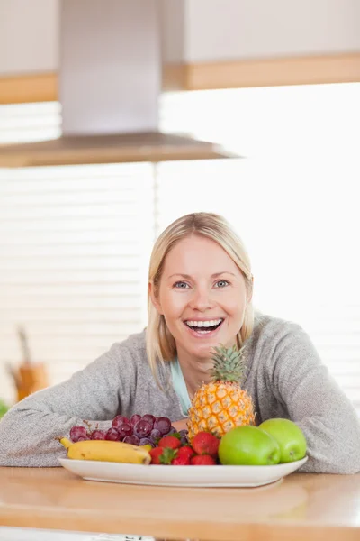 Mujer sonriente sentada detrás de un plato de frutas —  Fotos de Stock