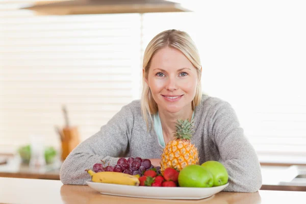 Mujer sentada en la cocina con un plato de frutas —  Fotos de Stock